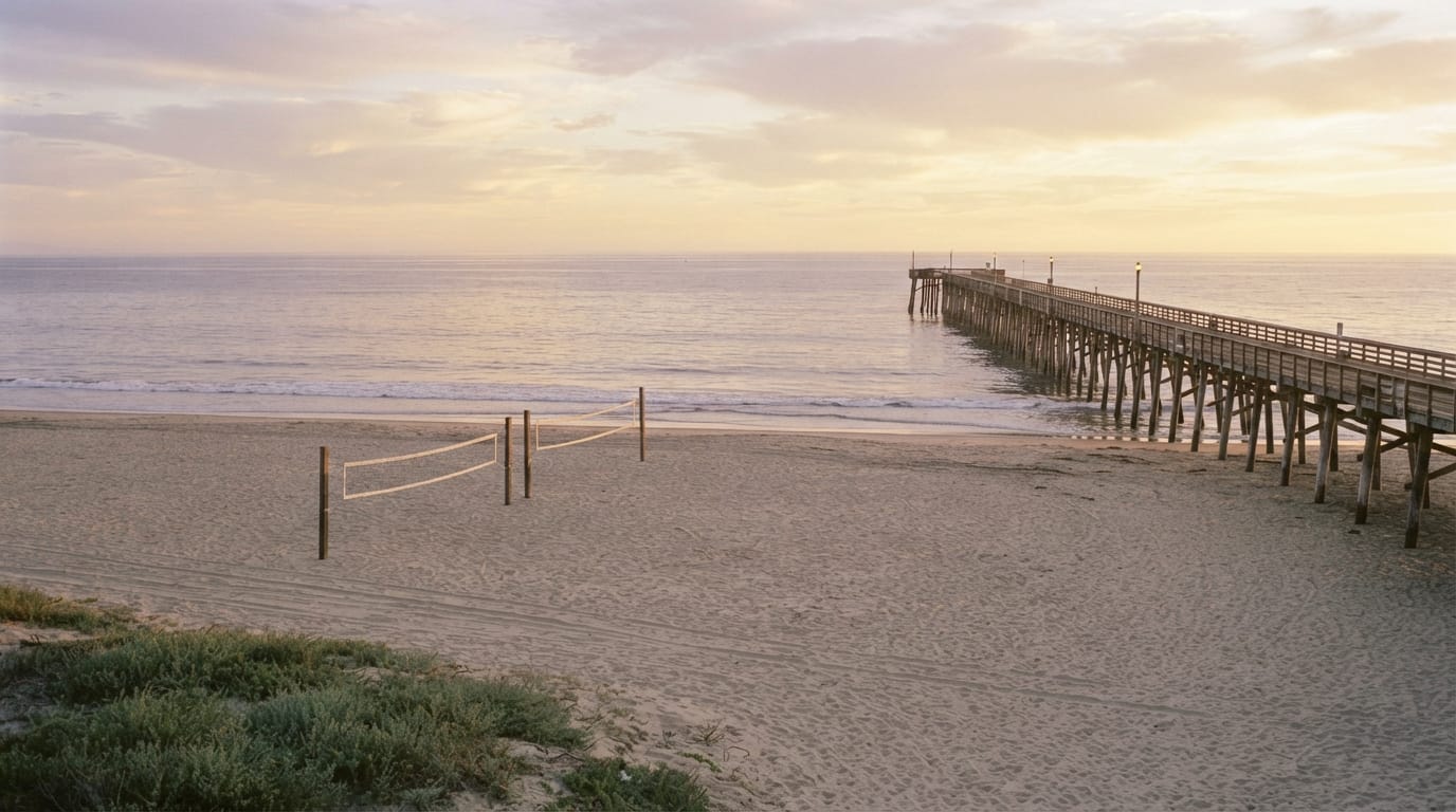 A wide pristine beach and pier at golden hour with volleyball nets on the sand, evoking Manhattan Beach